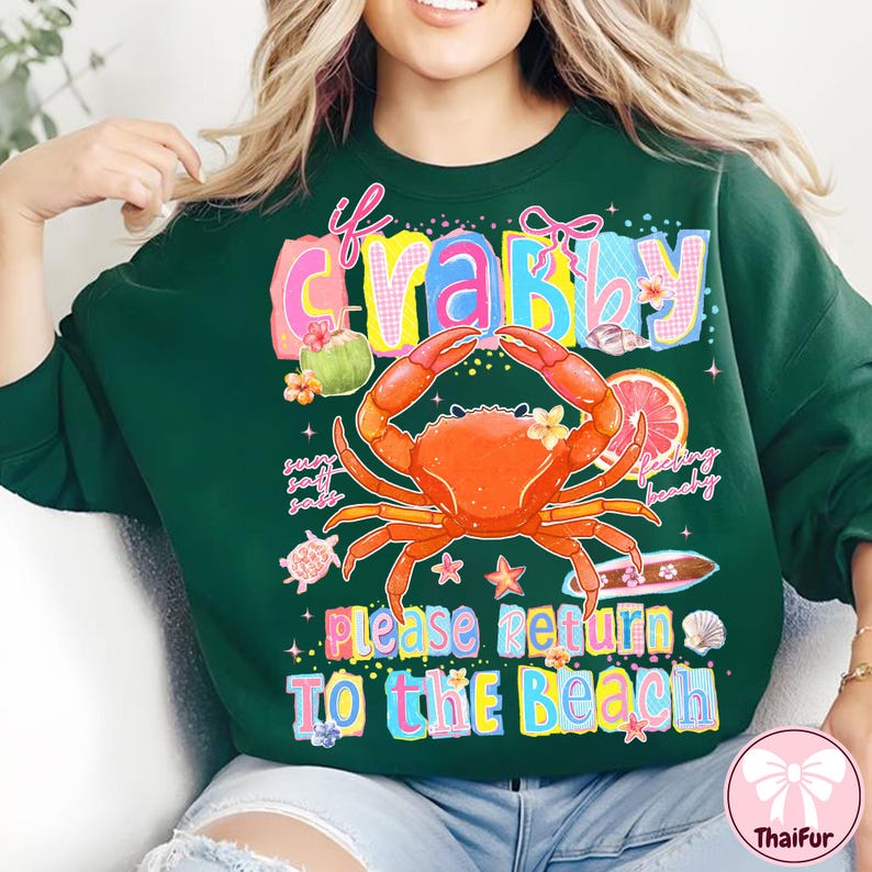 May include: Dark green sweatshirt featuring a crab graphic and the text "If Crabby, Please Return To The Beach". The crab is orange with yellow details, and the text is in bright colours. The sweatshirt has a crew neck.