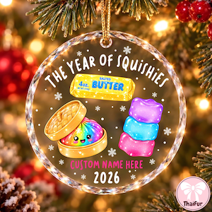 May include: A round, clear acrylic Christmas ornament featuring the text THE YEAR OF SQUISHIES, a yellow stick of salted butter, a rainbow-colored dumpling in a bamboo steamer, and three stacked colorful squishy toys with CUSTOM NAME HERE and 2026.