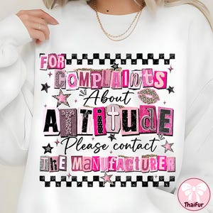 May include: White sweatshirt with the text "FOR COMPLAINTS ABOUT ATTITUDE Please contact THE MANUFACTURER" in pink, black, and leopard print lettering. The design includes stars and a checkered border.