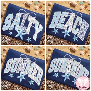 May include: Four navy blue t-shirts with beach-themed text: "Salty", "Beach", "Summer", and "Sunshine". Each word is in white and light blue, decorated with starfish and a pearl-like string. The shirts are on sand with seashells.