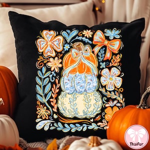 May include: Black decorative pillow featuring a stacked pumpkin design with orange, blue, and yellow floral accents. The pumpkins have a bow and floral patterns. The pillow is surrounded by pumpkins.