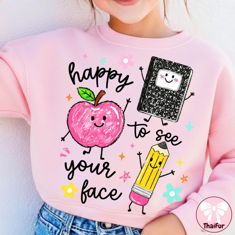 May include: A light pink sweatshirt featuring a graphic print of a smiling pink apple, a black and white composition notebook, and a yellow pencil. The text "happy to see your face" is printed in black script, surrounded by small colorful stars and flowers.