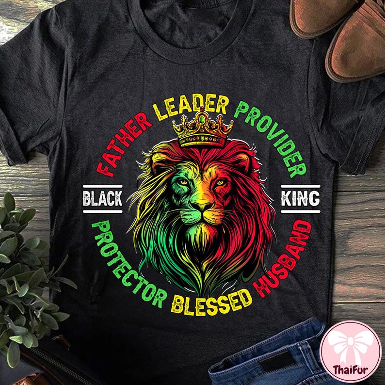 May include: Dark gray t-shirt featuring a lion's head with a crown, in red, yellow, and green. Text around the lion reads "Father, Leader, Provider, Protector, Blessed, Husband, King, Black."