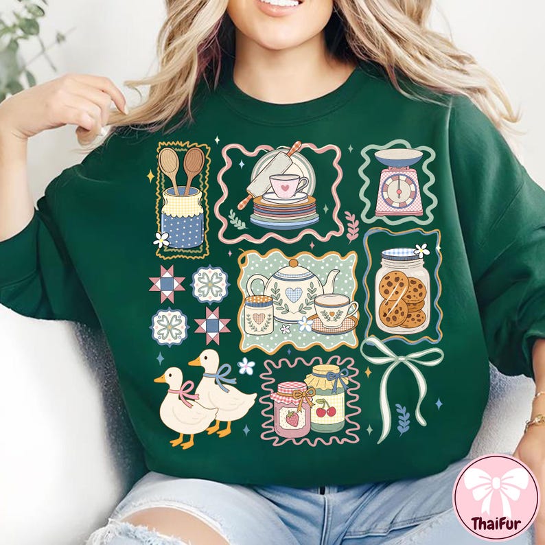 Peut inclure: Sweat-shirt vert fonc&eacute; avec un motif sur le th&egrave;me de la cuisine. Le motif comprend des illustrations d'ustensiles de cuisine, de tasses &agrave; th&eacute;, de biscuits et de canards. L'esth&eacute;tique g&eacute;n&eacute;rale est de style vintage.