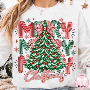 May include: A white sweatshirt featuring a central graphic of a green Christmas tree decorated with red ornaments and a large red and white striped bow. The text Merry Merry Christmas is printed in red and green with surrounding snowflakes.