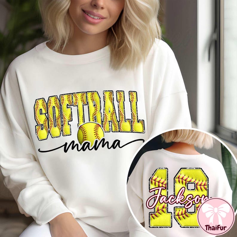Op de afbeelding: Cr&egrave;mekleurige sweatshirt met de woorden "SOFTBALL mama" in gele en zwarte letters, met een softbalafbeelding. De achterkant van de sweatshirt heeft het nummer 18 en de naam "Jackson" in een vergelijkbare stijl.