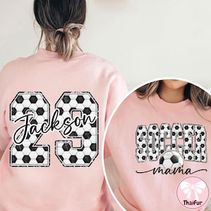 K&ouml;nnte beinhalten: Hellrosa Sweatshirt mit Fu&szlig;ball-Design. Das Sweatshirt hat die Nummer 29 mit dem Namen "Jackson". Ein weiteres Sweatshirt hat die Worte "Soccer Mama" mit einer Fu&szlig;ball-Grafik.