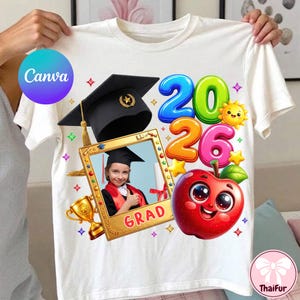 May include: White t-shirt featuring a graduation theme. The design includes the year "2026" in colorful bubble letters, a cartoon apple, a graduation cap, and a photo frame with a child wearing a graduation gown. The word "GRAD" is also visible.