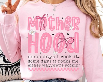 May include: Pink sweatshirt with the text "Mother Hood" in pink letters with black outlines and a pink bow. The text "some days I rock it, some days it rocks me, either way we're rockin'" is printed below the main text.