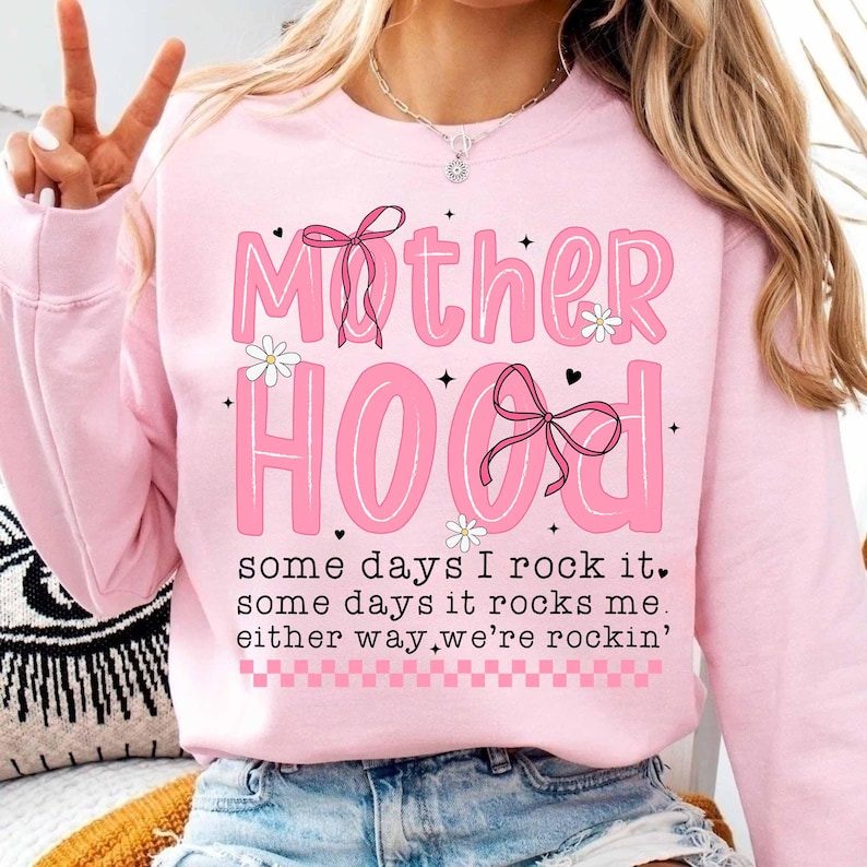 May include: Pink sweatshirt with the text "Mother Hood" in pink letters with black outlines and a pink bow. The text "some days I rock it, some days it rocks me, either way we're rockin'" is printed below the main text.