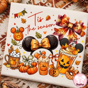 May include: A white fabric square featuring a colorful autumn-themed print with the text 'Tis the season'. The design includes pumpkin-shaped Mickey ears, a large patterned bow, a mug with marshmallows, a pumpkin-faced drink, and orange pumpkins.