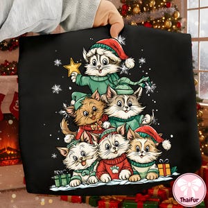 May include: Black pillow featuring a Christmas tree design made of six cartoon cats. The cats wear green sweaters and red Santa hats. One cat holds a gold star. Snowflakes and gifts are also included in the design.
