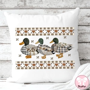 May include: White decorative pillow featuring three ducks with plaid and patchwork patterns. The ducks have green heads and yellow beaks. The pillow has a decorative border with hearts and plaid accents. The pillow is a home decor item.