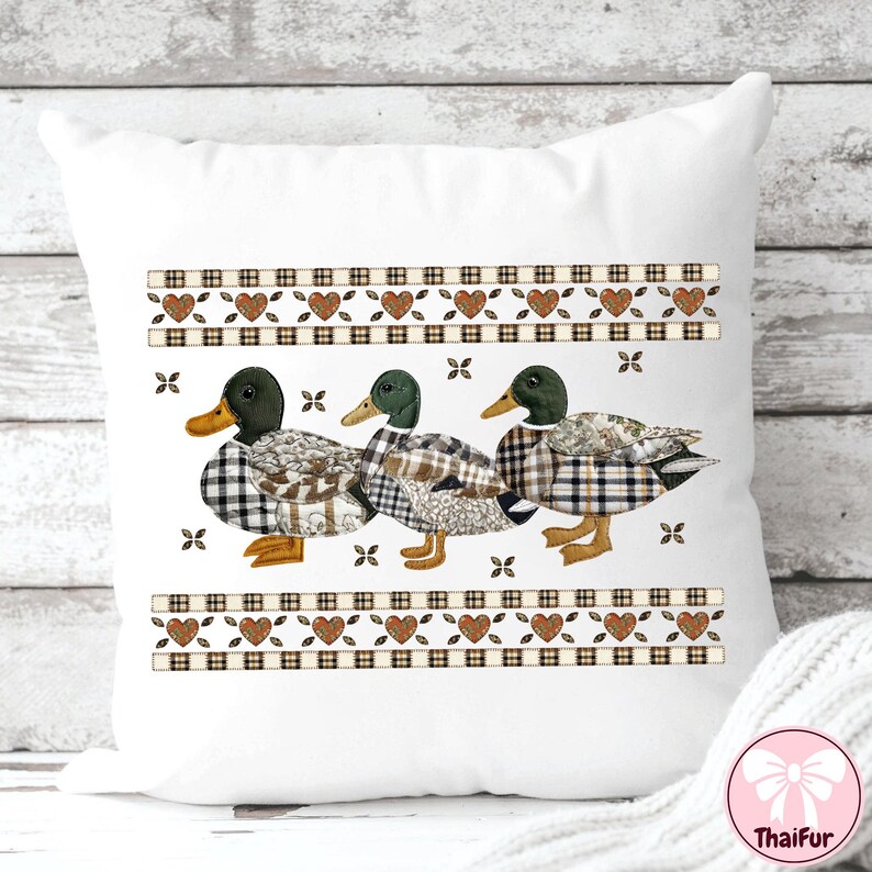 May include: White decorative pillow featuring three ducks with plaid and patchwork patterns. The ducks have green heads and yellow beaks. The pillow has a decorative border with hearts and plaid accents. The pillow is a home decor item.