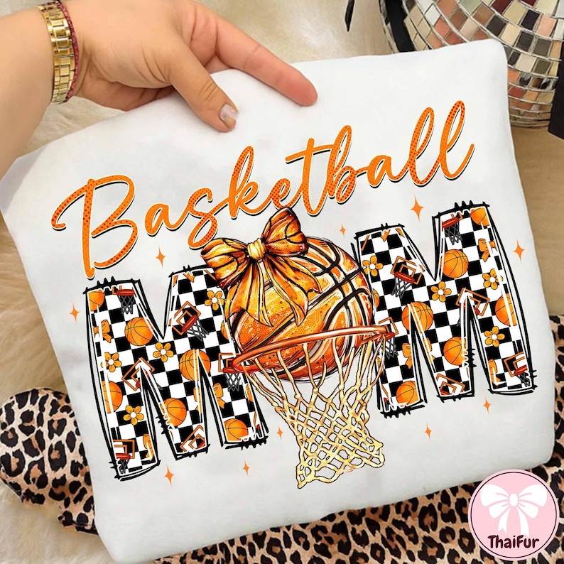 May include: White sweatshirt with an orange basketball design. The word "Basketball" is written in orange script above the image of a basketball and hoop. The word "MOM" is in a checkered pattern with basketballs and flowers.