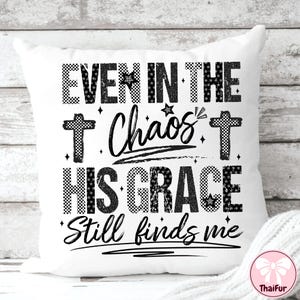 May include: White square pillow with the text "EVEN IN THE Chaos HIS GRACE Still finds me" in black. The text is in a mix of fonts and patterns, including checkered and star accents. Two crosses are also featured.