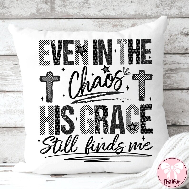 May include: White square pillow with the text "EVEN IN THE Chaos HIS GRACE Still finds me" in black. The text is in a mix of fonts and patterns, including checkered and star accents. Two crosses are also featured.