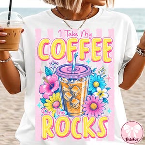 May include: White t-shirt with a colorful graphic of an iced coffee drink with the text "I Take My Coffee On The Rocks". The design includes pink, yellow, and blue flowers, and a pink striped background.