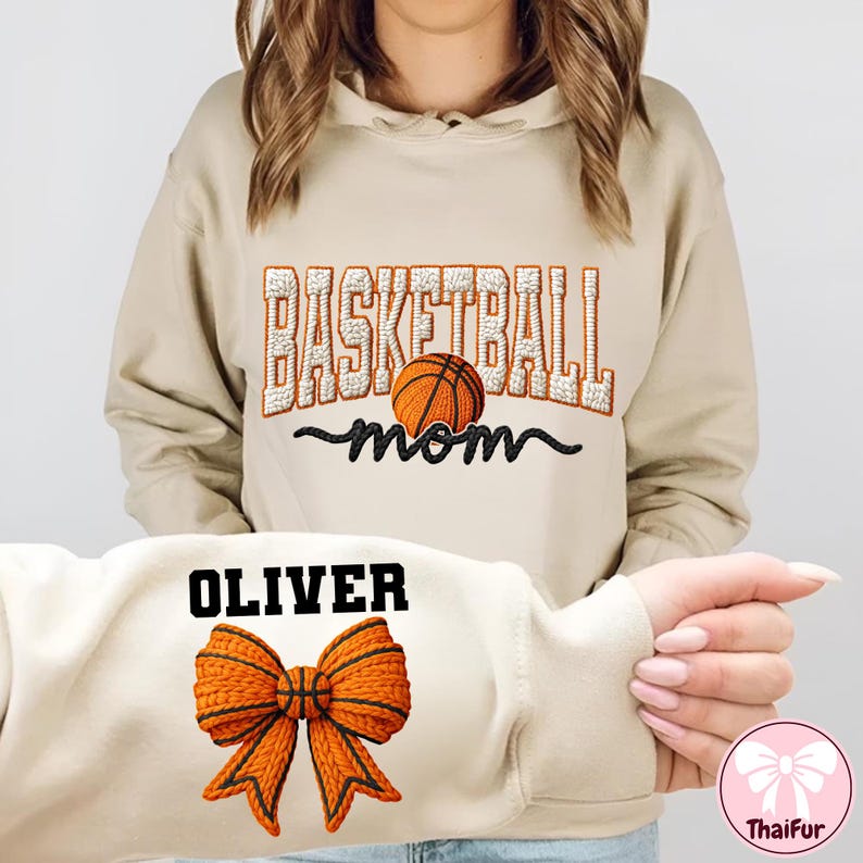 Puede incluir: Sudadera con capucha beige con el texto "BASKETBALL mom" y un gr&aacute;fico de baloncesto. La parte inferior de la sudadera muestra el nombre "OLIVER" y un lazo con un dise&ntilde;o de baloncesto. La sudadera es de color neutro.