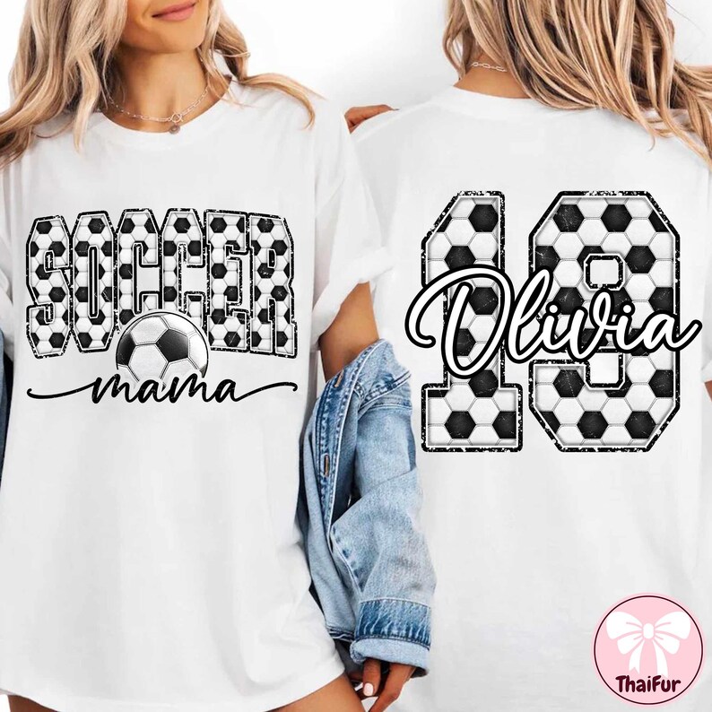 K&ouml;nnte beinhalten: Wei&szlig;es T-Shirt mit "Soccer Mama" in Schwarz und Fu&szlig;ballgrafiken auf der Vorderseite. Auf der R&uuml;ckseite befindet sich die Nummer 10 mit einem Fu&szlig;ballmuster und dem Namen "Olivia" in Schreibschrift.