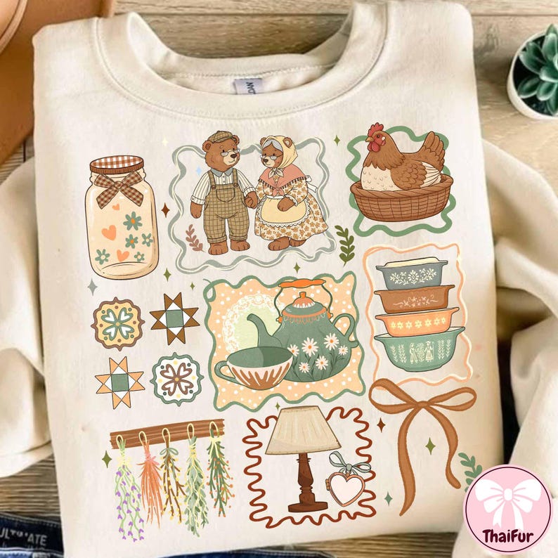 Może przedstawiać: Kremowa bluza z r&oacute;żnymi ilustracjami. Projekty obejmują słoik, misie, kurę w koszu, filiżanki, miski, lampę i kokardę. Grafika ma estetykę vintage i wiejską.