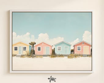 May include: A framed print featuring four colorful beach huts in pastel shades of yellow, pink, and blue, set against a sandy beach and a light blue sky with fluffy clouds. The artwork is signed by Blue Coastal Collective.