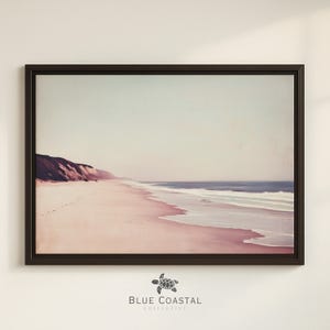 Könnte beinhalten: Ein gerahmter Druck einer Strandszene. Das Bild zeigt einen rosafarbenen Sandstrand, einen blauen Ozean und einen hellblauen Himmel. Der Druck ist in einem dunkelbraunen Rahmen. Die Worte "BLUE COASTAL COLLECTIVE" stehen unten.