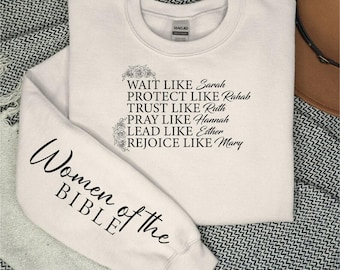 May include: A cream-colored sweatshirt with black text that reads "Women of the Bible" on the left sleeve and "Wait like Sarah, Protect like Rahab, Trust like Ruth, Pray like Hannah, Lead like Esther, Rejoice like Mary" on the right side.