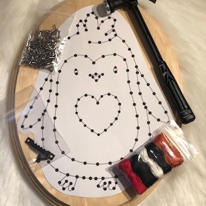 May include: A wooden craft kit with a penguin design. It includes a hammer, nails, and coloured thread. The penguin outline is printed on white paper, ready for nail art. A saw-tooth hanger is included.