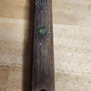 Op de afbeelding: Een close-up van de handgreep van een schilmes. De handgreep is gemaakt van donker hout met twee groene accenten. De handgreep heeft een gat aan de onderkant.
