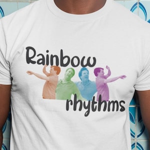 Peut inclure: Un t-shirt blanc avec un graphique de quatre personnes dans un schéma de couleurs arc-en-ciel. Le texte "Rainbow rhythms" est imprimé sous le graphique.