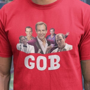 May include: A red t-shirt with a collage of images of a man with different expressions. The text "GOB" is printed below the images.