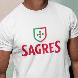 May include: White t-shirt with the red word "SAGRES" and a green and red shield logo. The shirt is worn by a person wearing sunglasses and blue jeans.