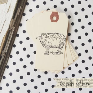 May include: A stack of blank gift tags with a brown paper hole punch. The top tag features a black and white line drawing of a sheep. The text "the polka dot baker" is visible at the bottom of the image.