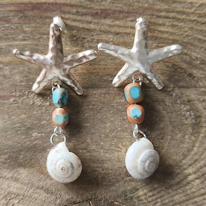 May include: A pair of drop earrings featuring a silver-toned starfish stud at the top. Below each starfish, two small, round, multi-coloured turquoise and orange beads are connected to a single, small, white spiral seashell charm at the base.
