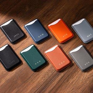 Könnte beinhalten: Acht rechteckige Kartenhalter in verschiedenen Farben, darunter Schwarz, Marineblau, Orange und Grau. Jeder Kartenhalter hat einen weißen Akzent und personalisierten Text oder Symbole. Der Markenname "Casebellé" ist oben abgebildet.