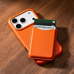 May include: Orange leather phone case with a card holder attached. The case is on a wooden surface. The card holder contains several cards. The phone case has a white camera section with three lenses.