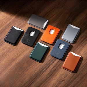 May include: A collection of leather cardholders in various colors, including black, gray, orange, green, and brown, arranged on a wooden surface. Each cardholder features a white accent and a unique design element, with some having a cutout.