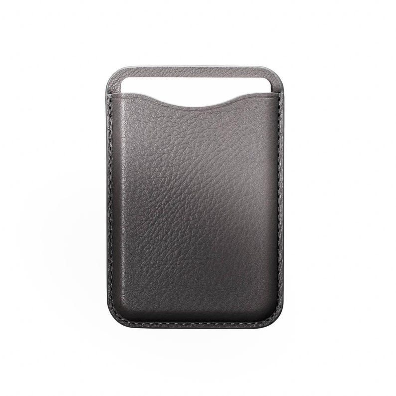 May include: A gray leather phone sleeve with a handle at the top. The sleeve has a textured surface and a curved opening for easy access to the phone. The stitching is visible along the edges.