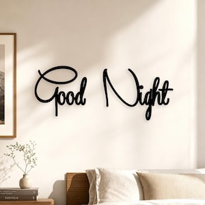 May include: A black wall-mounted sign featuring the words Good Night written in a continuous, flowing cursive script. The lettering is composed of thin, dark lines that stand out against the light-colored wall surface behind the text.