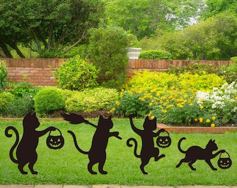 Może przedstawiać: Cztery czarne sylwetki kotów z motywami Halloween są wyświetlane na zielonym trawniku. Każdy kot trzyma wiadro z dyniową latarnią lub miotłę czarownicy. Tło przedstawia ceglany mur, bujną zieleń i różnorodne kwiaty.