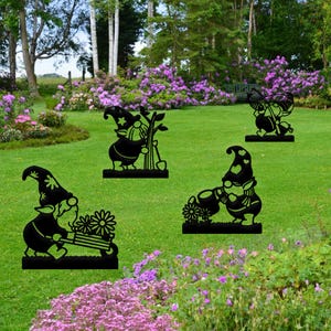 May include: Four black metal garden gnome silhouettes with different poses. The gnomes are holding gardening tools, a watering can, and a wheelbarrow. The gnomes are standing on a green lawn with flowers in the background.