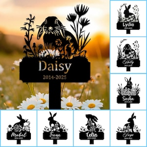 May include: Black metal garden stakes with rabbit silhouettes and floral details. Each stake displays a name and dates, such as "Daisy 2014-2025". These decorative stakes are designed for outdoor use in gardens.