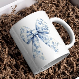 May include: White ceramic mug with a blue and white floral patterned bow design.