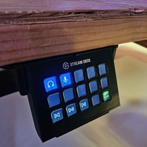 May include: A black Stream Deck with a variety of buttons, including a headphone icon, a microphone icon, and a play button. The buttons are illuminated with blue and green lights.