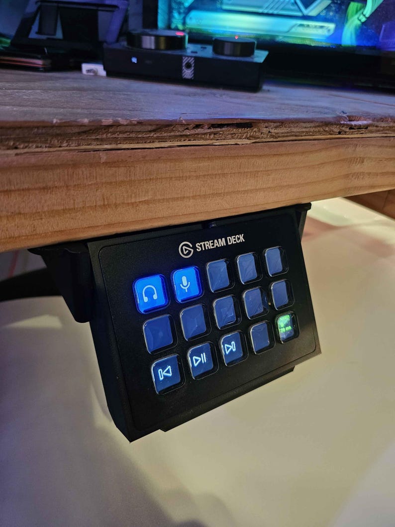 May include: A black Stream Deck with a blue lit headphone icon and a microphone icon. The deck has 15 buttons with various icons, including play, pause, and fast forward.