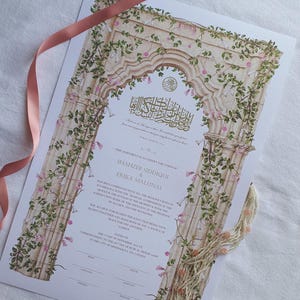 May include: A wedding certificate featuring an illustration of a stone archway covered in green vines and pink flowers. The document includes printed text with the names Shahzeb Siddiqui and Erika Malunas, along with a pink ribbon and beaded tassel.