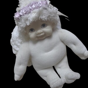 Puede incluir: Una mu&ntilde;eca de querub&iacute;n blanca con una cara de porcelana y un cuerpo suave y afelpado. La mu&ntilde;eca tiene ojos azules, una expresi&oacute;n dulce y un halo con una cinta rosa. Es un art&iacute;culo decorativo.