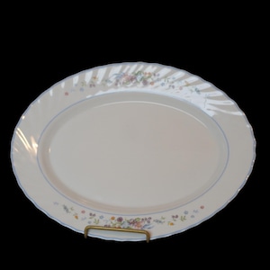 Könnte beinhalten: Eine ovale, weiße Servierplatte mit hellblauem Rand und floralem Design. Der Rand hat eine wellenförmige Kante. Die Platte wird von einem goldfarbenen Metallständer getragen. Das florale Design umfasst rosa, lila und gelbe Blumen.