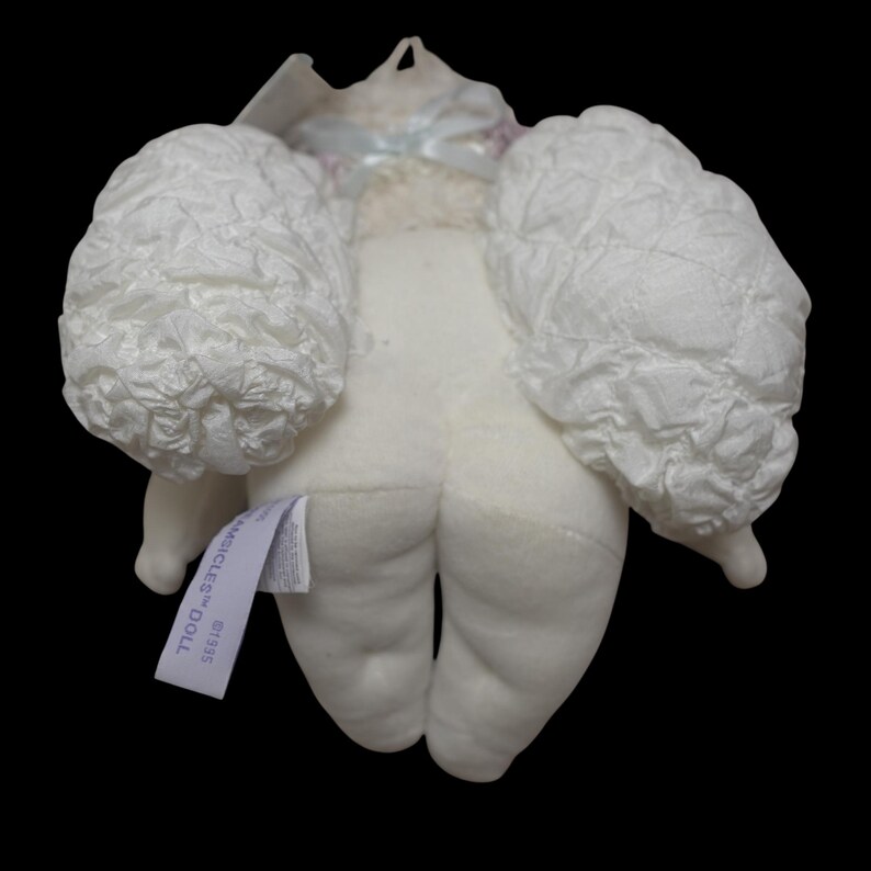 Puede incluir: Una mu&ntilde;eca de peluche blanca con alas blancas adjuntas. La mu&ntilde;eca tiene una etiqueta que dice "AMICICLES DOLL". La mu&ntilde;eca est&aacute; hecha de tela suave y tiene un dise&ntilde;o simple. Las alas tienen textura y a&ntilde;aden un toque caprichoso.